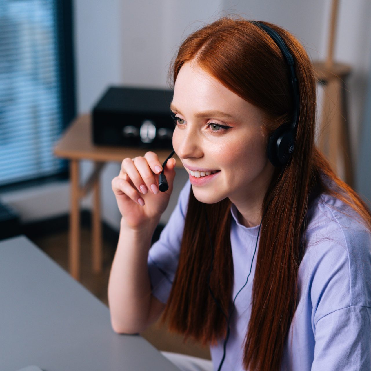 Lachende medewerker met headset aan haar laptop, klaar om je te helpen
